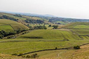 roulant vert collines avec patchwork des champs en dessous de une brumeux ciel, représentant rural les terres agricoles paysage. photo
