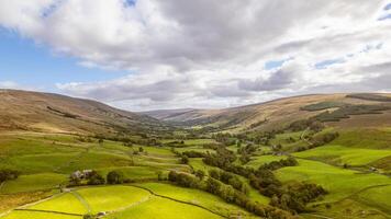 scénique vue de une luxuriant vert vallée avec patchwork des champs et roulant collines en dessous de une nuageux ciel. photo