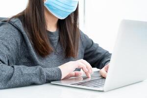 femme utilisant un ordinateur portable sur le bureau à la maison avec un masque pour protéger covid-19 photo