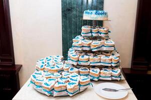 mariage banquet décoration sur le table avec blanc nappe de table. élégant bonbons bar avec savoureux Gâteaux dans blanc et bleu couleurs. gâteau supporter assortiment photo