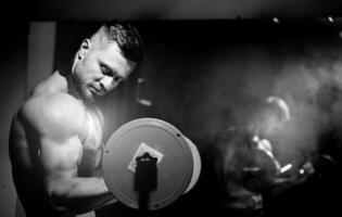 Beau brutal sexy fort bodybuilder athlétique aptitude homme pompage en haut muscles et levage haltère. la musculation concept. noir et blanc photo. vue de le côté fermer. photo