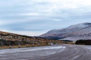 enroulement route par une neigeux Montagne paysage en dessous de couvert ciels. photo