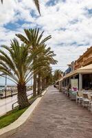 pittoresque bord de mer promenade avec paume des arbres et Extérieur les cafés en dessous de une nuageux ciel dans los chrétiens, tenerife. photo