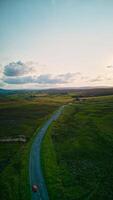 aérien vue de une scénique route enroulement par une luxuriant vert paysage avec une Célibataire rouge voiture, en dessous de une vaste ciel à crépuscule dans Yorkshire. photo