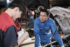 asiatique Masculin professionnel automobile ingénieur superviseur décrit voiture moteur entretien et réparation travail avec mécanicien ouvrier états-majors équipe dans réparer un service garage, spécialiste métiers dans auto industrie. photo