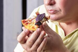 le homme mains tenir une pièce de Pizza à le sien bouche. photo