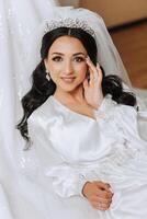 magnifique la mariée dans une pansement robe dans le Matin avant le mariage cérémonie. incroyable coiffure de le la mariée. Naturel et moderne se maquiller. portrait de une Jeune la mariée dans une pansement robe. photo