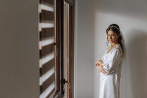 magnifique la mariée dans une pansement robe dans le Matin avant le mariage cérémonie. incroyable coiffure de le la mariée. Naturel et moderne se maquiller. portrait de une Jeune la mariée dans une pansement robe. photo