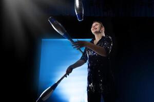 cirque actrice effectue. fille jongle avec masses sur une foncé Contexte dans le projecteurs. photo