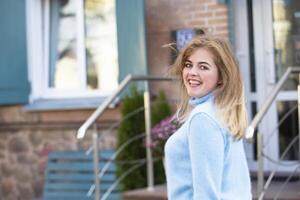 sur le rue, une content blond fille dans une bleu tricoté chandail. photo