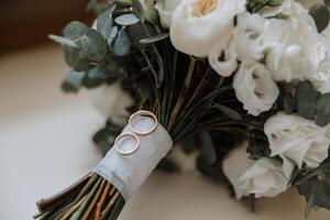 mariage bouquet. blanc Couper des roses, vert la graine têtes et feuilles. vert tiges et blanc ruban et or mariage anneaux. photo