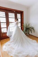 Jeune brunette dans longue mariage robe et voile dans Hôtel chambre. une charmant mariée, plein longueur, dans une magnifique blanc robe sur le Matin avant le mariage. photo