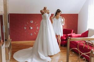 une magnifique la mariée avec une longue voile dans sa chambre, portant une peignoir. mariage robe sur une mannequin. le la mariée dans le Matin avant le mariage cérémonie. photo