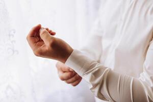 mains bouton en haut le boutons sur le sien chemise. le processus de fixation le boutons sur le sien blanc chemise. proche voir. jeune marié boutons sur le sien chemise menottes. Matin de le jeune marié photo