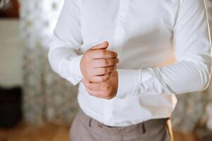 mains bouton en haut le boutons sur le sien chemise. le processus de fixation le boutons sur le sien blanc chemise. proche voir. jeune marié boutons sur le sien chemise menottes. Matin de le jeune marié photo