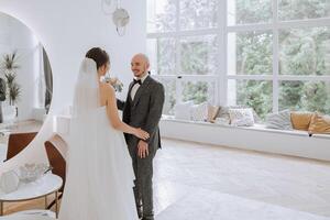 le la mariée est habillé dans un élégant luxuriant blanc mariage robe avec une longue voile et est prêt pour sa jeune marié. le premier réunion de le la mariée et jeune marié photo