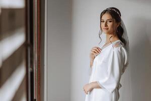 magnifique la mariée dans une pansement robe dans le Matin avant le mariage cérémonie. incroyable coiffure de le la mariée. Naturel et moderne se maquiller. portrait de une Jeune la mariée dans une pansement robe. photo