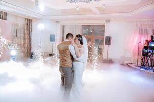 mariage Danse de le la mariée et jeune marié. le premier Danse de le la mariée et jeune marié dans un élégant mariage salle avec le utilisation de lourd fumée et pyrotechnique lumières, confettis. photo