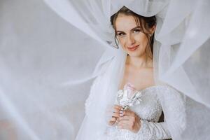 magnifique Jeune la mariée en portant voile dans blanc mariage robe, portrait de brunette la mariée dans Hôtel chambre, Matin avant mariage. photo