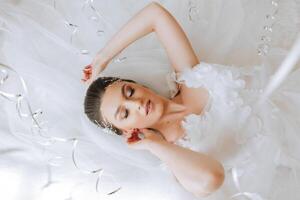 une magnifique Jeune la mariée fille est mensonge dans une magnifique peignoir. Matin de le la mariée avant le mariage cérémonie. photo