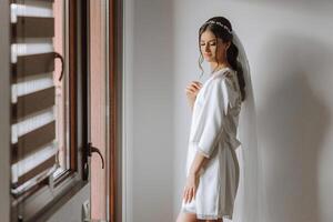 magnifique la mariée dans une pansement robe dans le Matin avant le mariage cérémonie. incroyable coiffure de le la mariée. Naturel et moderne se maquiller. portrait de une Jeune la mariée dans une pansement robe. photo