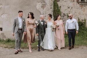 le la mariée et jeune marié avec leur copains pose sur le vieux mur. une magnifique et élégant robe de le la mariée. élégant mariage. été mariage dans la nature photo