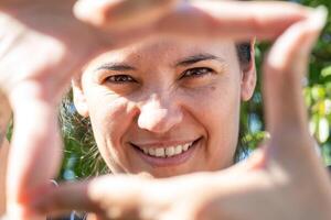 Naturel Latin femme sans pour autant maquillage fabrication une Cadre avec sa des doigts. elle est souriant et spontané. photo