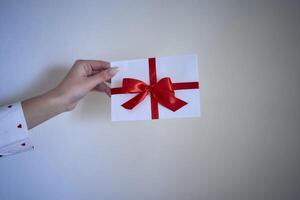 cadeau certificat dans rouge et blanc couleurs dans femelle mains sur une blanc mur Contexte photo