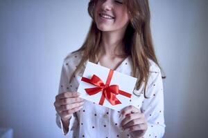 cadeau certificat dans le mains de une adolescent fille portant blanc pyjamas avec rouge cœurs photo