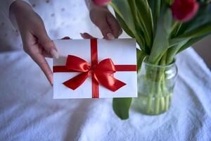 cadeau certificat dans rouge et blanc couleurs dans femelle mains avec rouge tulipes photo