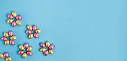 fleur en forme de pile de Pâques bonbons des œufs enveloppé dans rose et d'or déjouer sur bleu Contexte photo