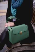 portrait de une élégant vieux femme dans une noir manteau avec vert accessoires sur une printemps rue photo