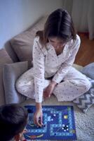 mère avec adolescent fille et peu fils dans pyjamas en jouant planche Jeux sur le sol photo