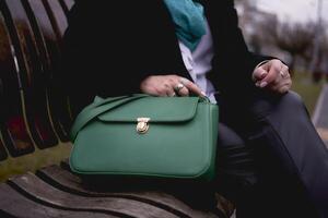 portrait de une élégant vieux femme dans une noir manteau avec vert accessoires sur une printemps rue photo