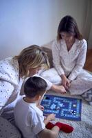 mère avec adolescent fille et peu fils dans pyjamas en jouant planche Jeux sur le sol photo