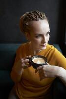 portrait de une élégant âge moyen femme dans une Jaune chandail en buvant café dans une café photo
