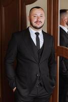 portrait de une Jeune jeune marié à Accueil avant le mariage cérémonie. une Beau homme habillé dans une classique costume. Masculin portrait. photo