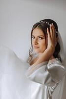 magnifique la mariée dans une pansement robe dans le Matin avant le mariage cérémonie. incroyable coiffure de le la mariée. Naturel et moderne se maquiller. portrait de une Jeune la mariée dans une pansement robe. photo