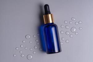 Vide bleu verre essentiel pétrole bouteille avec pipette sur gris Contexte décoré gouttes d'eau. peau se soucier concept avec Naturel produits de beauté photo