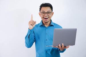 asiatique homme avec des lunettes sorti ou content avoir Nouveau des idées par montrer du doigt doigt en haut et en portant portable portant bleu chemise isolé sur blanc Contexte photo