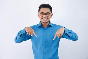 Beau asiatique Masculin employé avec des lunettes souriant dans doigt montrer du doigt vers le bas pose portant bleu chemise isolé sur blanc Contexte photo