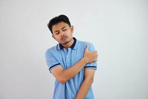 Jeune asiatique homme bleu t chemise geste douleur le sien épaule ou bras dans douleur isolé sur blanc Contexte photo