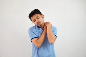 une portrait de Jeune asiatique homme ayant a cou et épaule douleur portant bleu t chemise isolé sur blanc Contexte photo
