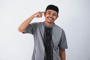 souriant Jeune asiatique musulman homme montrer du doigt à tête avec doigt génial idée ou Mémoire concept. portant koko vêtements isolé sur blanc Contexte photo