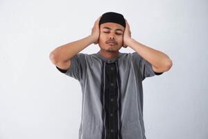 portrait Jeune musulman asiatique homme couvertures le sien oreilles, il Est-ce que ne pas vouloir à Ecoutez à quoi que ce soit, le gars à Accueil sur auto-isolement, portant koko vêtements isolé sur blanc Contexte photo