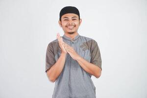 souriant Jeune asiatique musulman homme applaudir dans mains et à la recherche à caméra portant gris koko vêtements isolé sur blanc Contexte photo