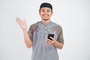 content ou souriant Jeune asiatique musulman homme en portant téléphone cellulaire portant koko vêtements isolé sur blanc Contexte. Ramadan concept photo