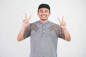 souriant ou content Jeune asiatique musulman homme montrant montrer du doigt en haut avec les doigts nombre deux tandis que sur de soi et montrant paix signe avec les doigts portant koko vêtements isolé sur blanc Contexte photo