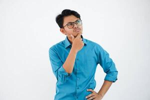 Jeune Beau asiatique homme avec des lunettes en pensant et à la recherche pour des idées tandis que en portant le menton portant bleu chemise isolé sur blanc Contexte photo