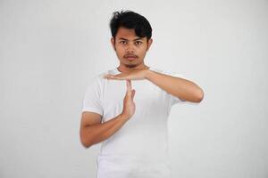sérieux Jeune asiatique homme donnant temps en dehors main geste portant blanc t chemise isolé sur blanc Contexte photo